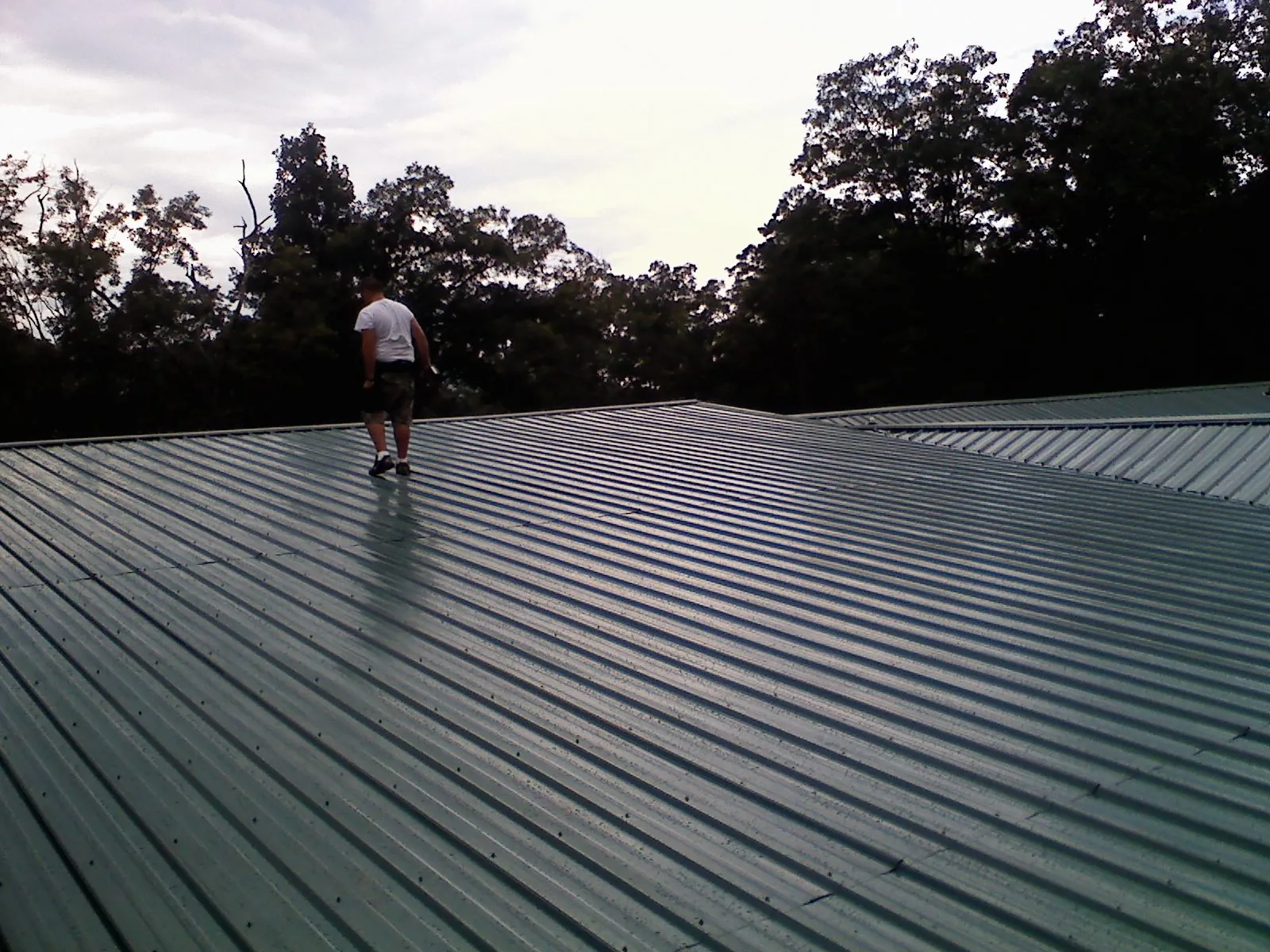 Roofer walking a wide expanse of new green metal roofing in Lawrence