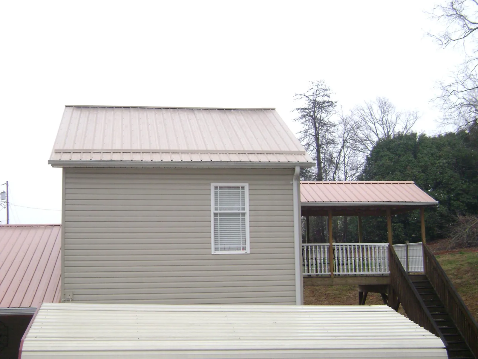 Tan metal roofs on a two story addition and attached porch, from a Roof Replacement job in Lawrence